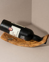 A curved olive wood wine holder holding a wine bottle, displayed against a neutral background.